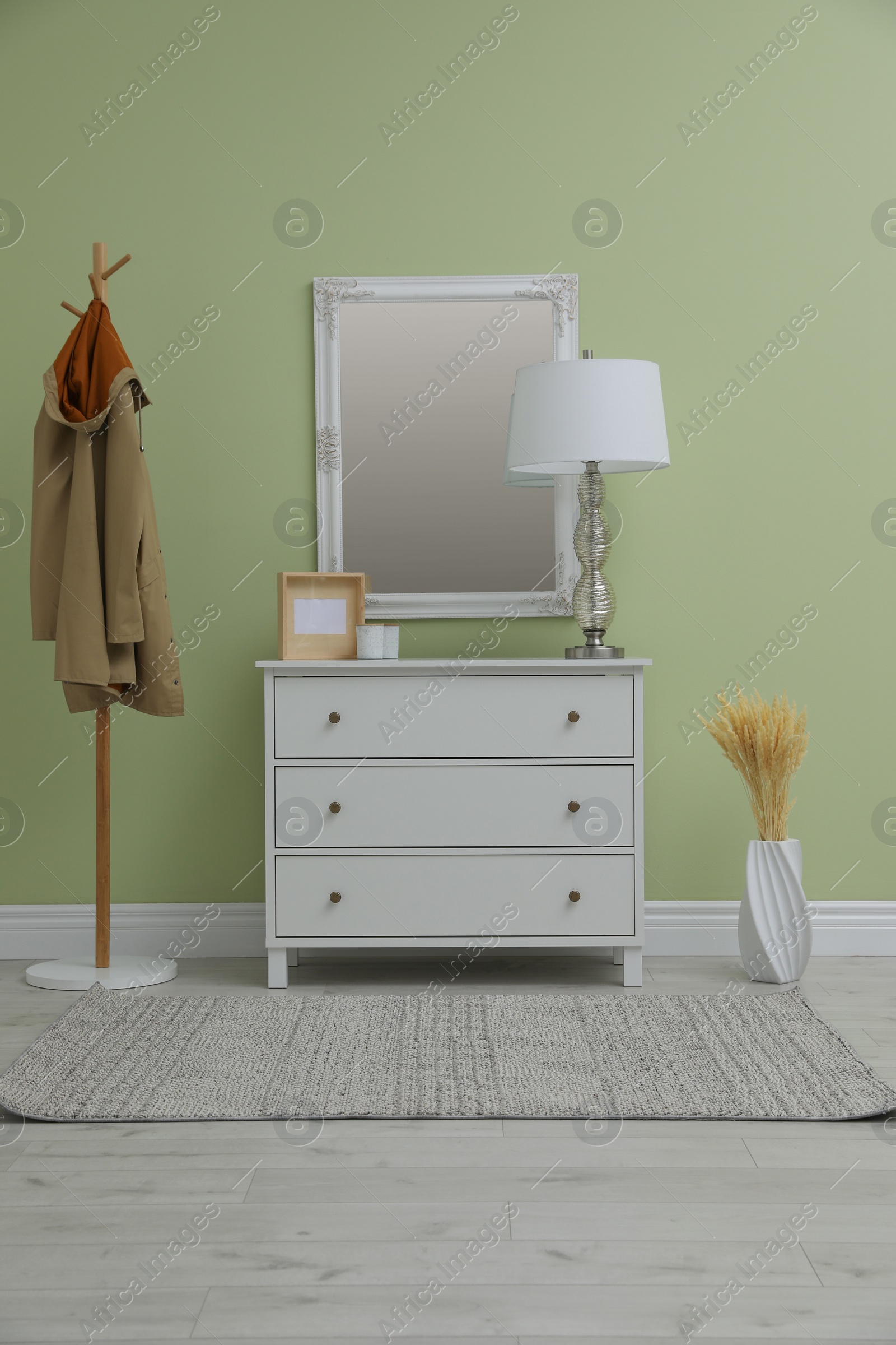 Photo of White chest of drawers with decor, coat stand and mirror in hallway. Interior design