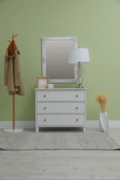 Photo of White chest of drawers with decor, coat stand and mirror in hallway. Interior design