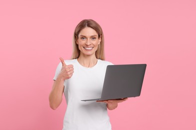 Photo of Happy woman with laptop showing thumb up on pink background