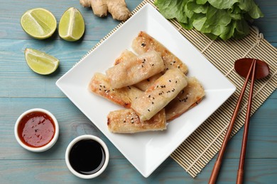 Photo of Tasty fried spring rolls served on light blue wooden table, flat lay