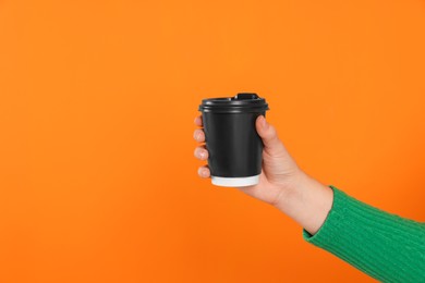 Photo of Woman holding takeaway cup with drink on orange background, closeup view and space for text. Coffee to go