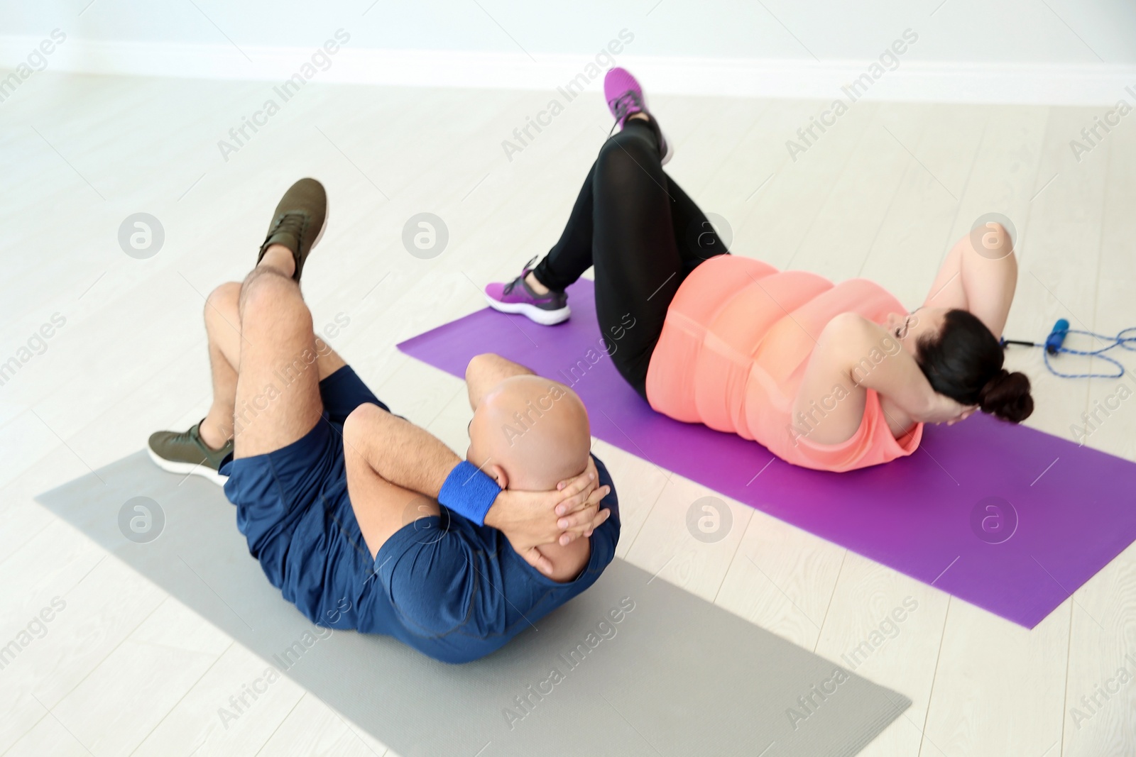 Photo of Overweight man and woman doing exercise on mats in gym