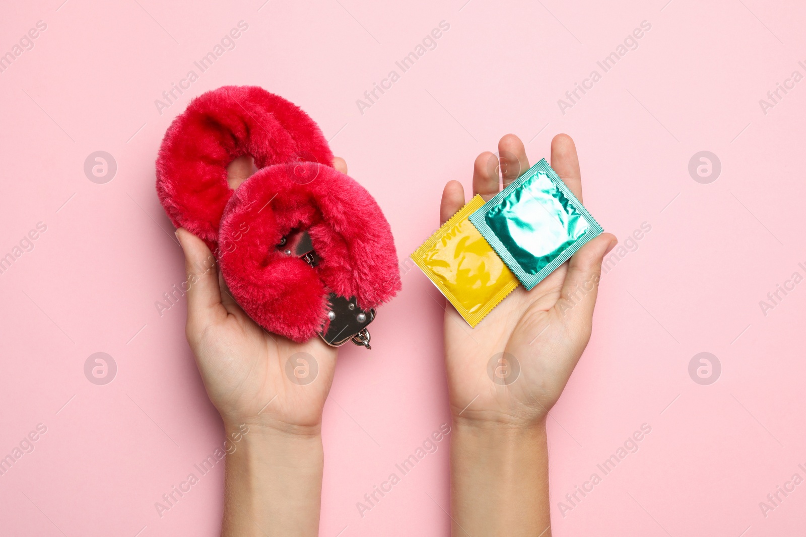 Photo of Woman with furry handcuffs and condoms on pink background, top view. Sex game