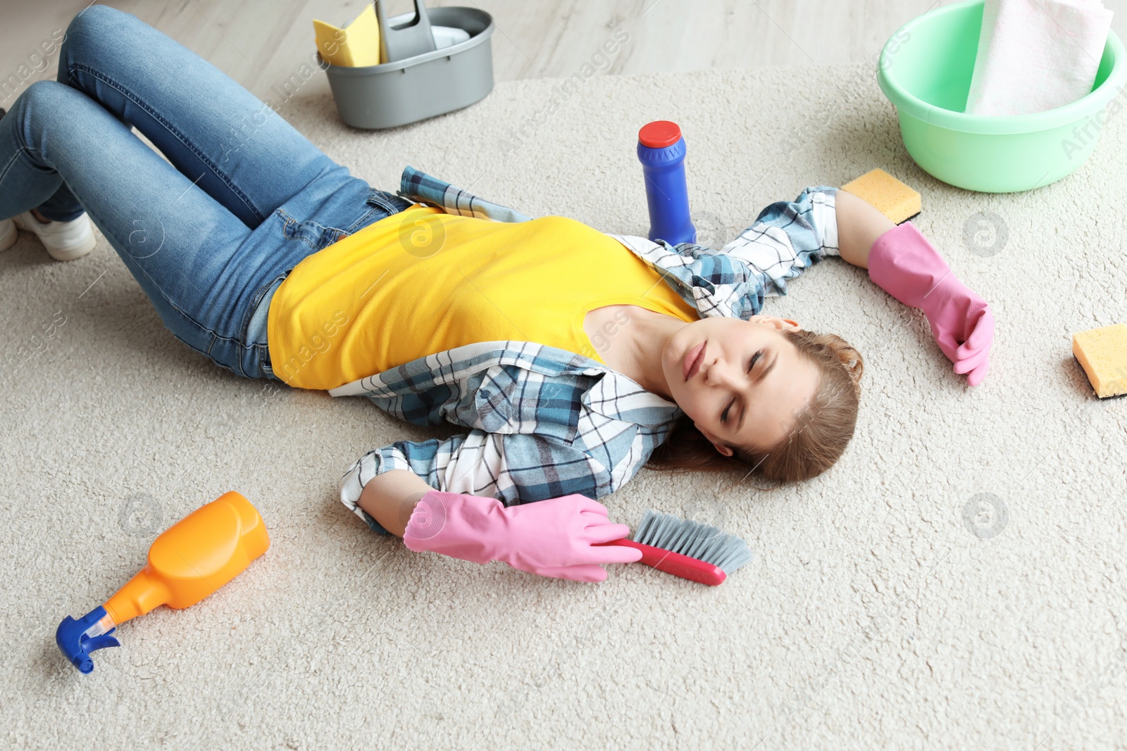 Photo of Tired woman with cleaning supplies lying on carpet at home
