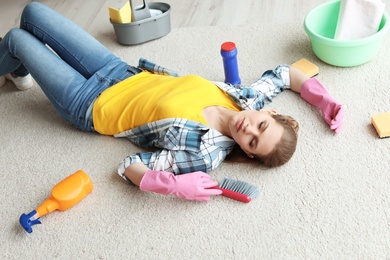 Tired woman with cleaning supplies lying on carpet at home