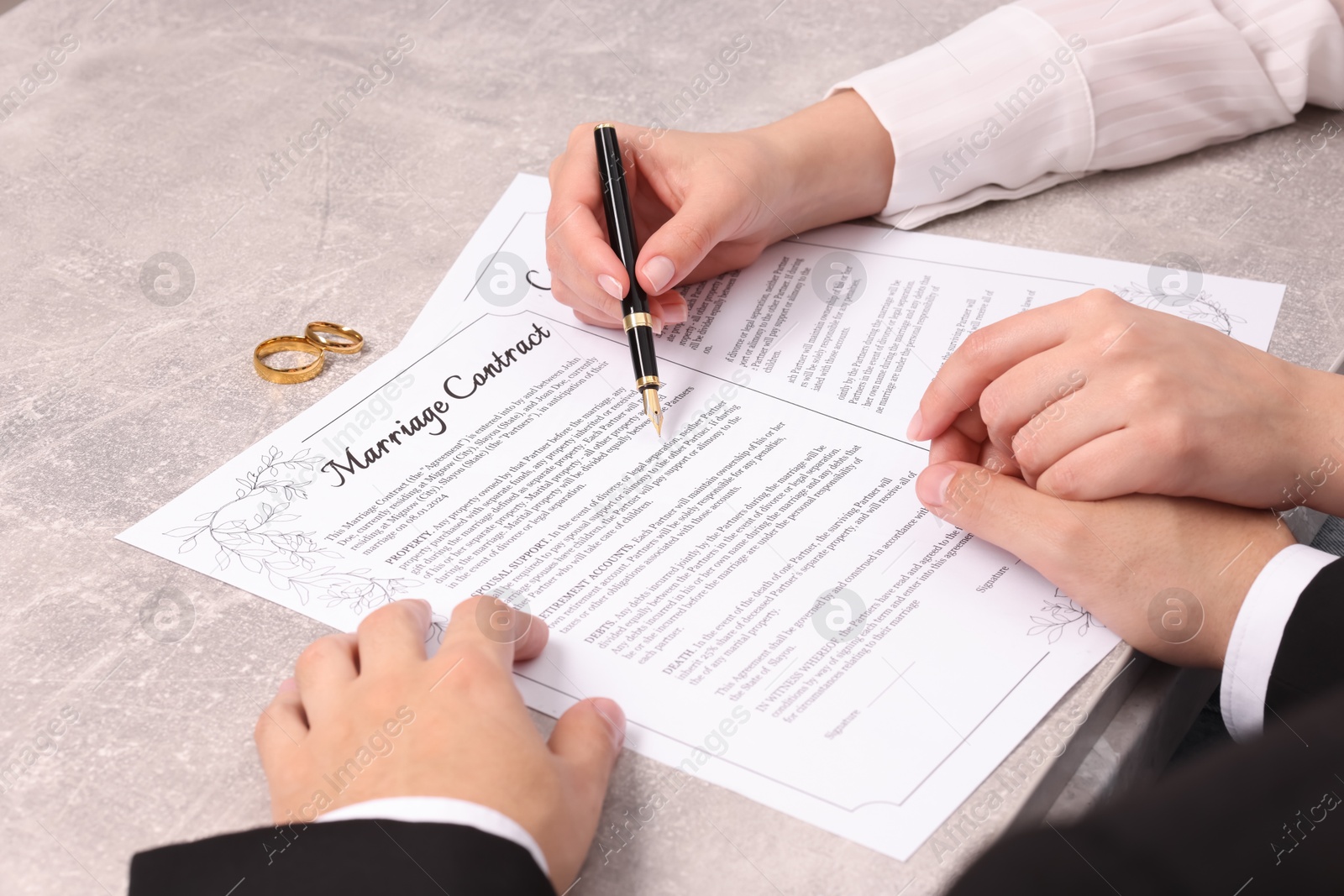 Photo of Man and woman signing marriage contract at light grey table, closeup