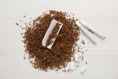 Photo of Heap of tobacco, paper, filters and hand rolled cigarettes on white wooden table, flat lay
