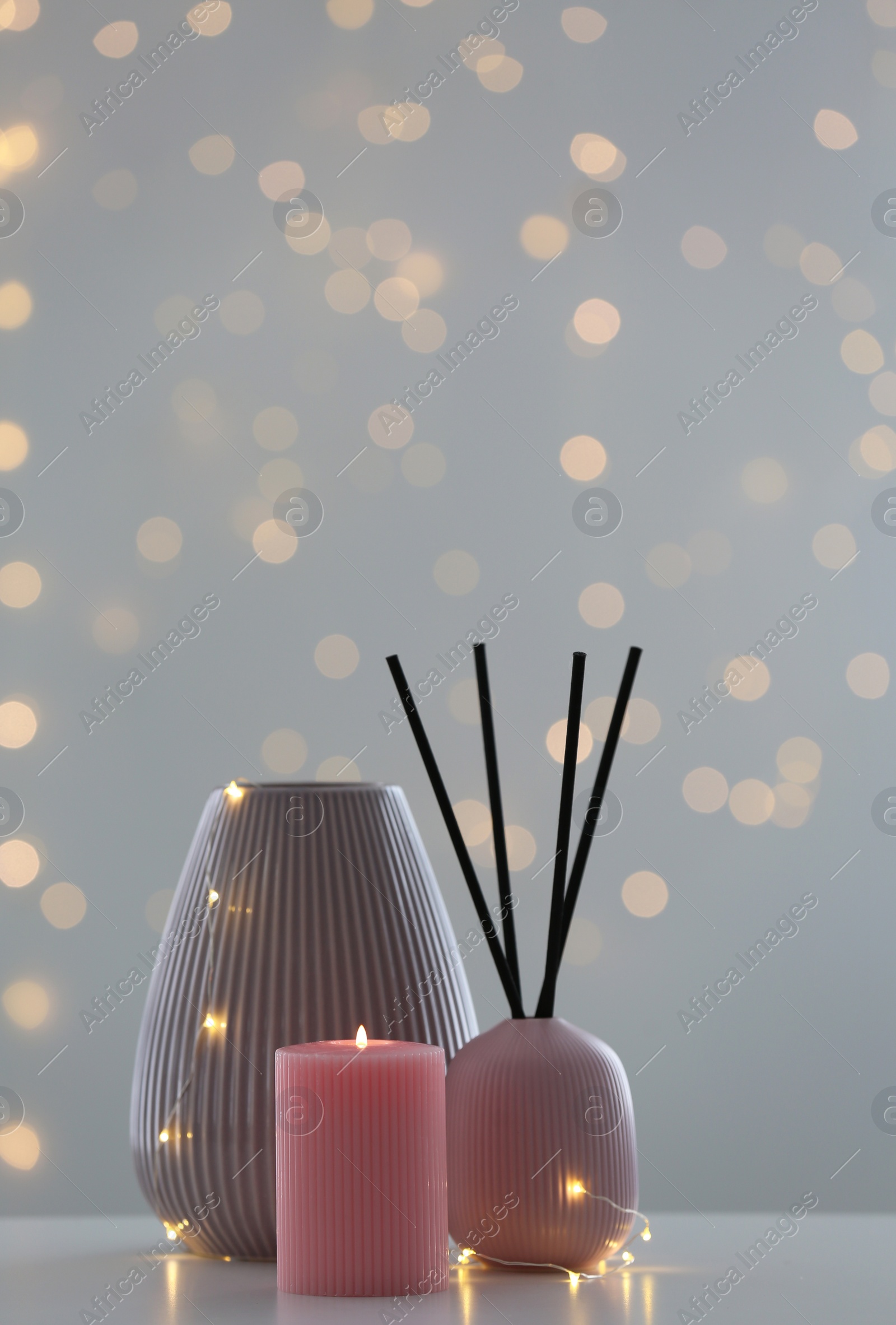 Photo of Vase, burning candle and reed diffuser on table against blurred background with bokeh effect. Space for text