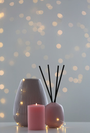 Vase, burning candle and reed diffuser on table against blurred background with bokeh effect. Space for text