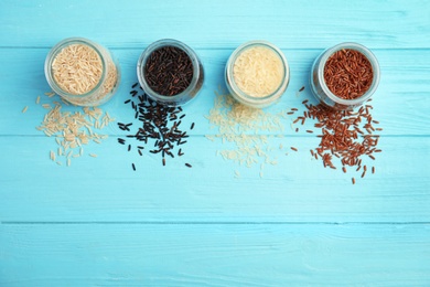 Jars with different types of rice on blue wooden background, top view. Space for text