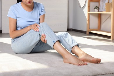 Photo of Young woman rubbing sore leg at home, closeup