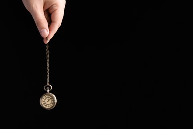 Photo of Closeup of psychotherapist with pendulum on black background, space for text. Hypnotherapy session