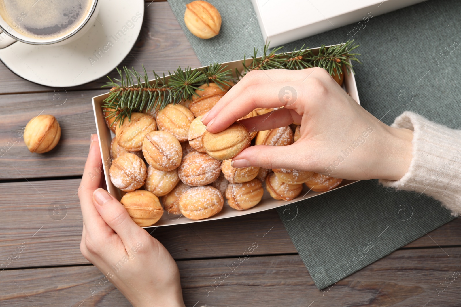 Photo of Woman taking delicious nut shaped cookies from box at wooden table, top view