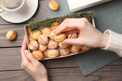 Woman taking delicious nut shaped cookies from box at wooden table, top view