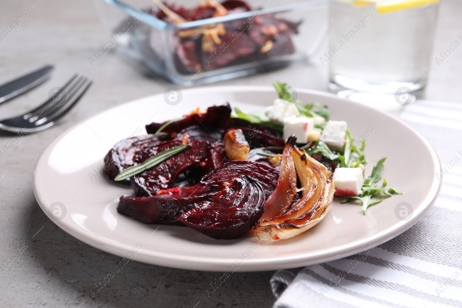 Photo of Roasted beetroot slices with, onion feta cheese and arugula on light grey table, closeup