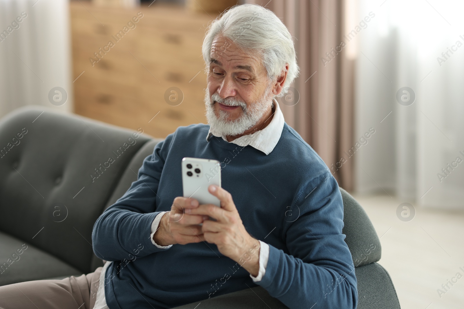 Photo of Portrait of happy grandpa using smartphone indoors