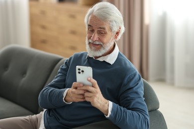 Portrait of happy grandpa using smartphone indoors