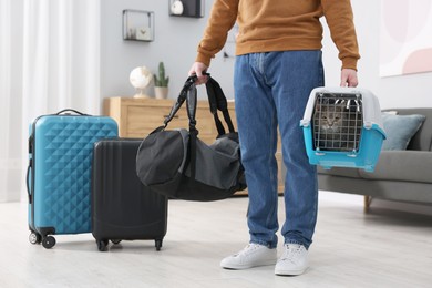 Photo of Travel with pet. Man holding carrier with cute cat and bag at home, closeup
