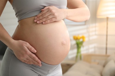 Photo of Pregnant young woman touching belly at home, closeup. Space for text