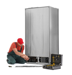 Male technician repairing refrigerator on white background