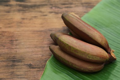 Delicious purple bananas and fresh leaf on wooden table, closeup. Space for text