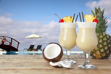 Tasty Pina Colada cocktail and ingredients on wooden table near outdoor swimming pool, space for text