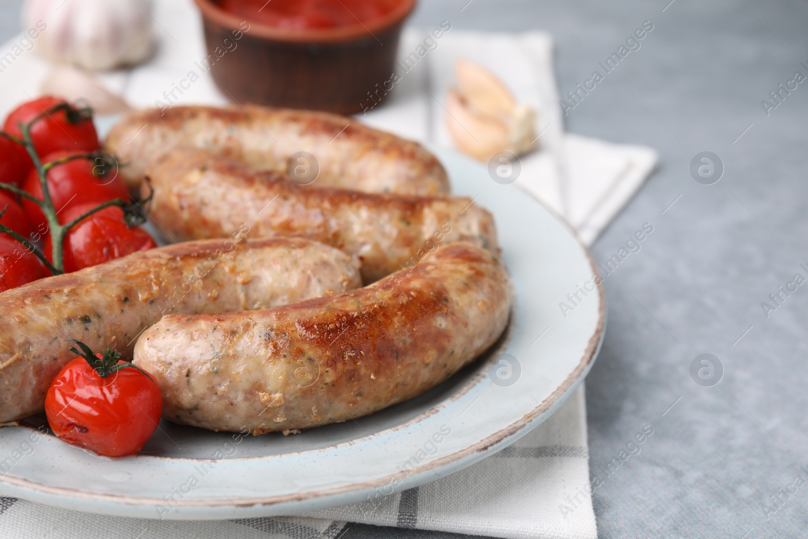 Photo of Plate with tasty homemade sausages and tomatoes on grey textured table, closeup. Space for text