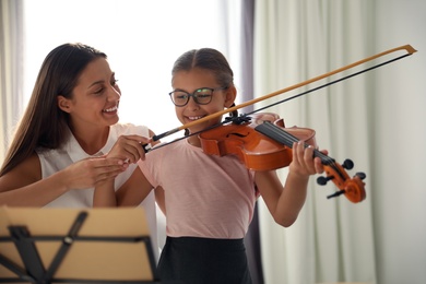 Young woman teaching little girl to play violin indoors