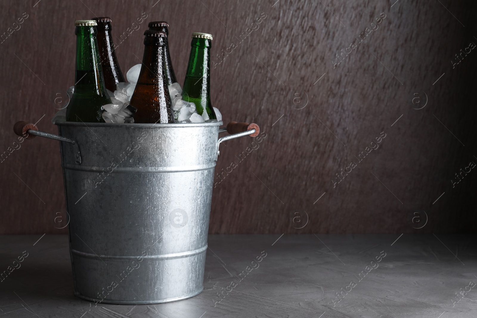 Photo of Metal bucket with bottles of beer and ice cubes on grey table, space for text