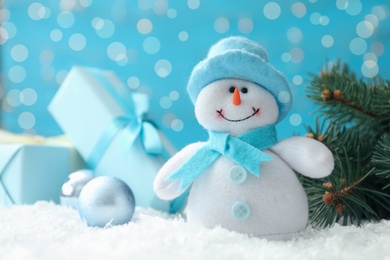 Snowman toy, fir tree and Christmas ball on snow against blurred festive lights, closeup