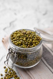 Photo of Glass jar with green mung beans on white textured table, closeup