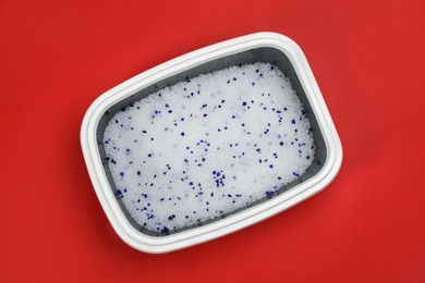 Cat litter tray with filler on red background, top view