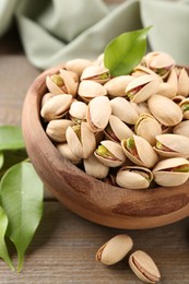 Delicious pistachios in bowl on wooden table, closeup