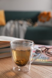 Glass cup of freshly brewed tea on wooden table in living room. Cozy home atmosphere