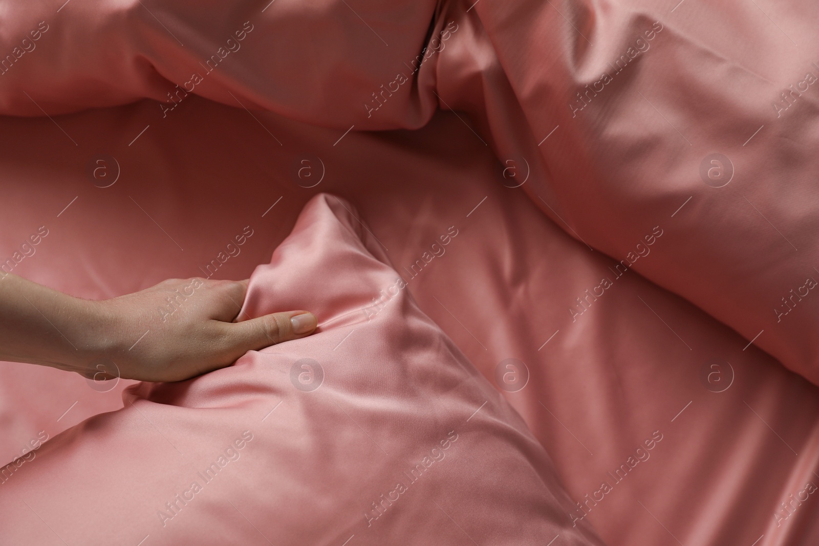 Photo of Woman making bed with beautiful pink silk linens, closeup view