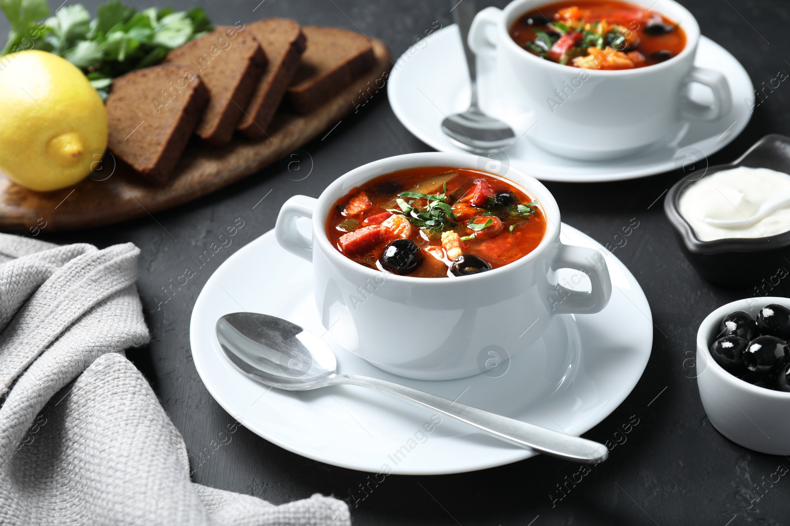 Photo of Meat solyanka soup with sausages and olives served on dark grey textured table