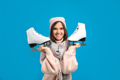 Happy woman with ice skates on light blue background