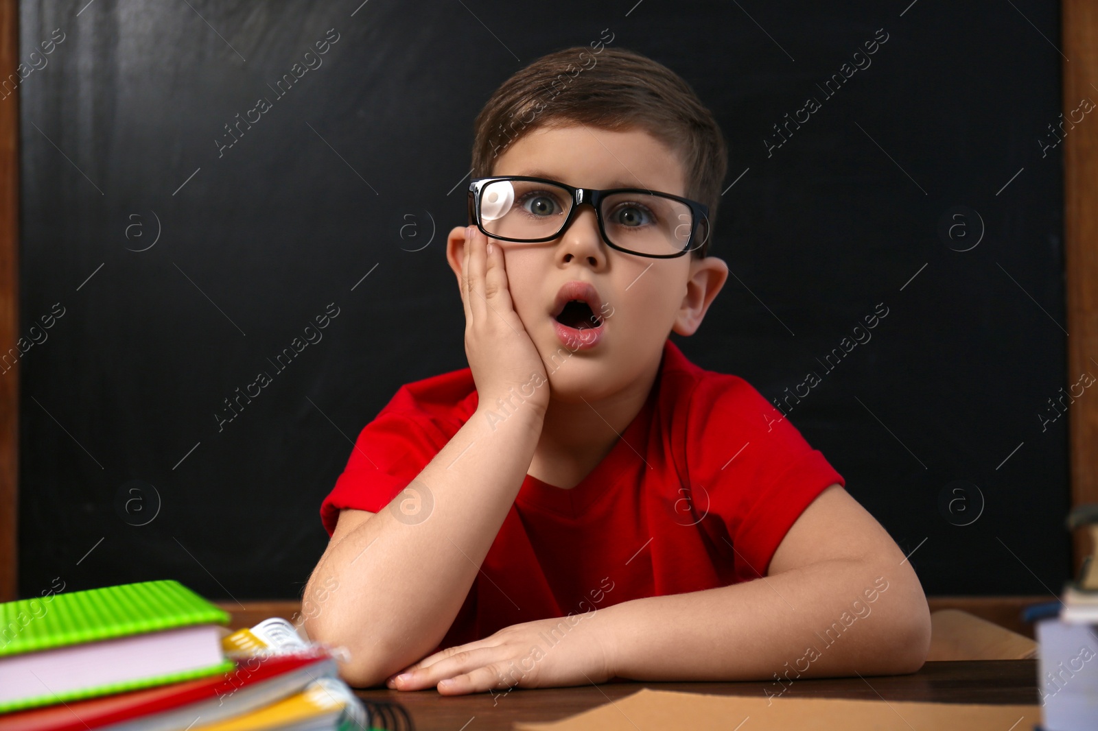 Photo of Cute little child wearing glasses at desk in classroom. First time at school