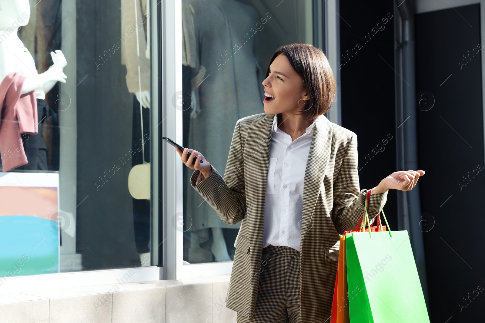Photo of Special Promotion. Emotional young woman with shopping bags and smartphone near showcase