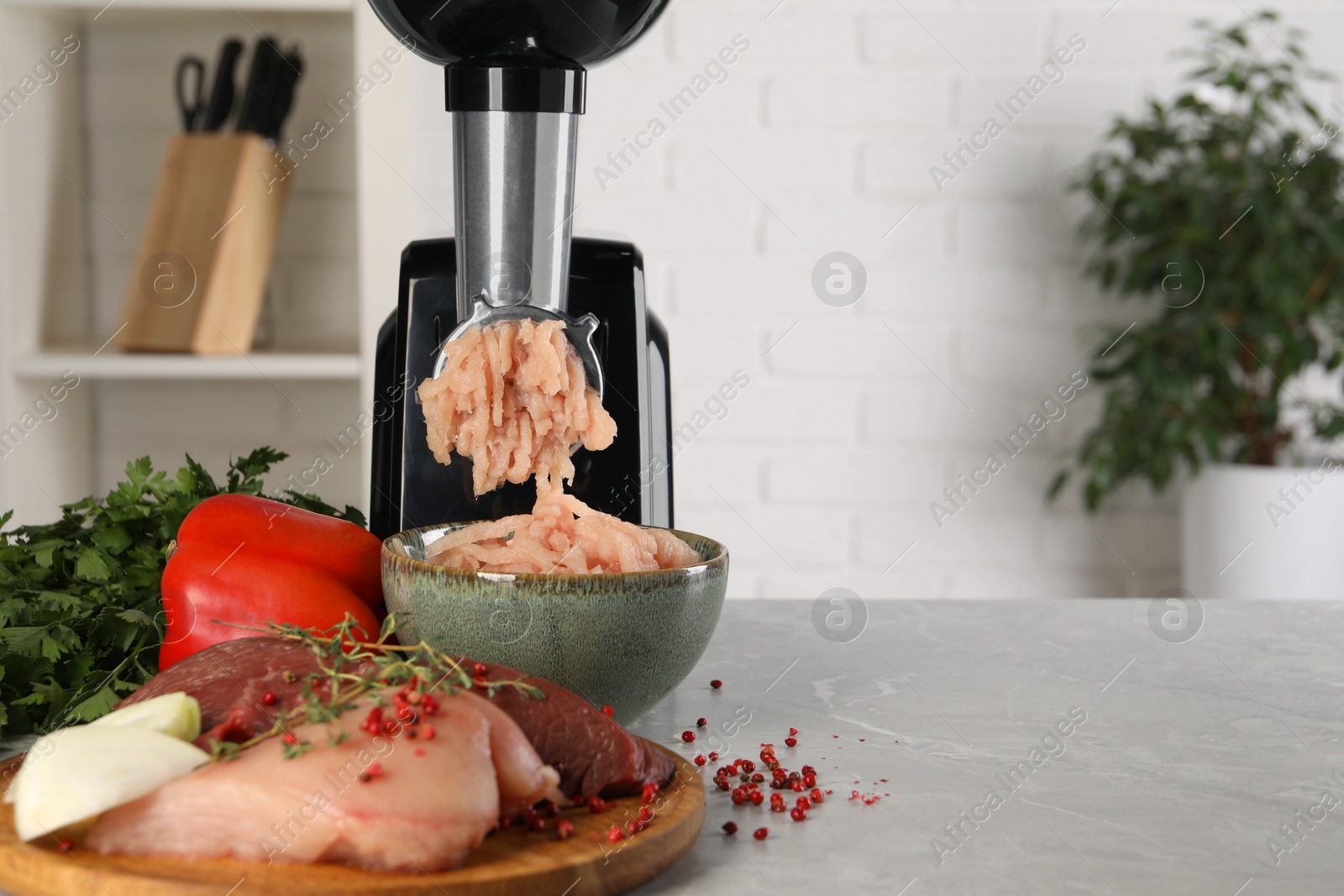 Photo of Electric meat grinder with chicken mince and products on grey marble table indoors. Space for text