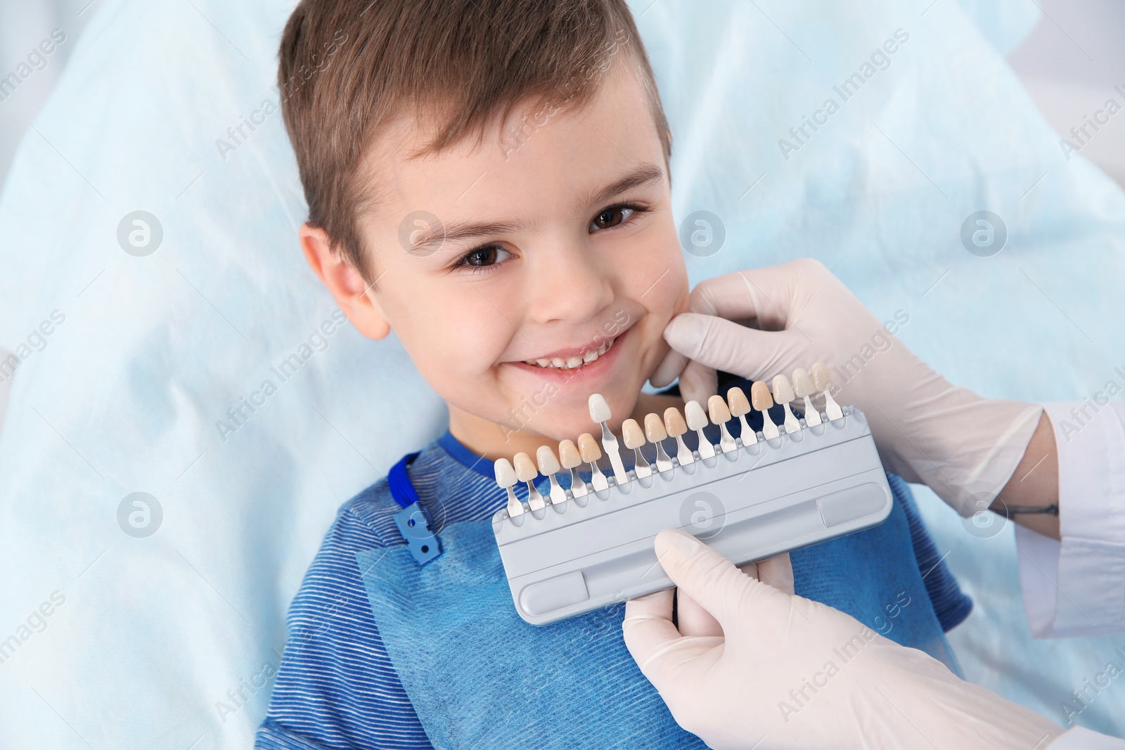 Photo of Dentist selecting cute boy's teeth color with palette in clinic