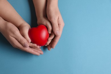 Mother and her child holding red decorative heart on light blue background, top view. Space for text