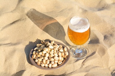Glass of cold beer and pistachios on sandy beach, above view