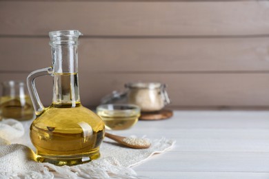 Photo of Jug of organic sesame oil on white wooden table. Space for text