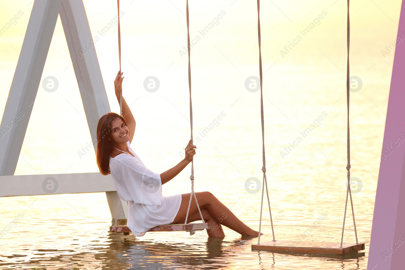 Photo of Young woman enjoying sunrise on swing over water