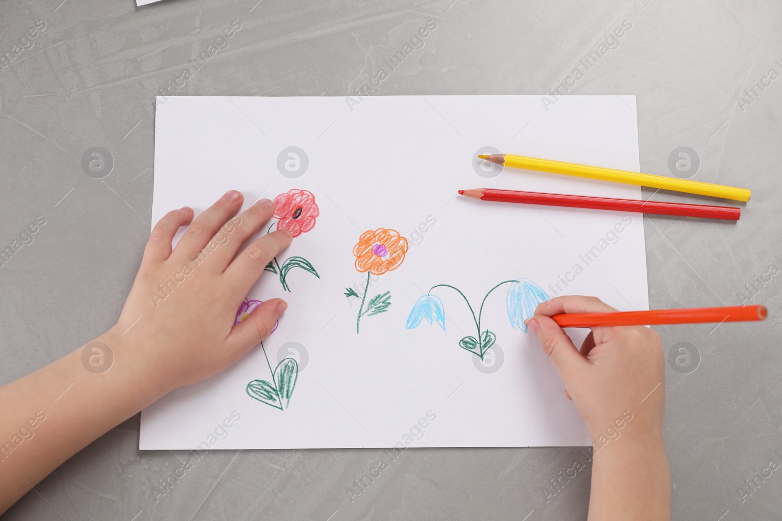 Photo of Little boy drawing flowers with pencil at grey textured table, top view. Child`s art