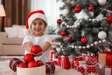 Cute little girl with box of Christmas balls at home