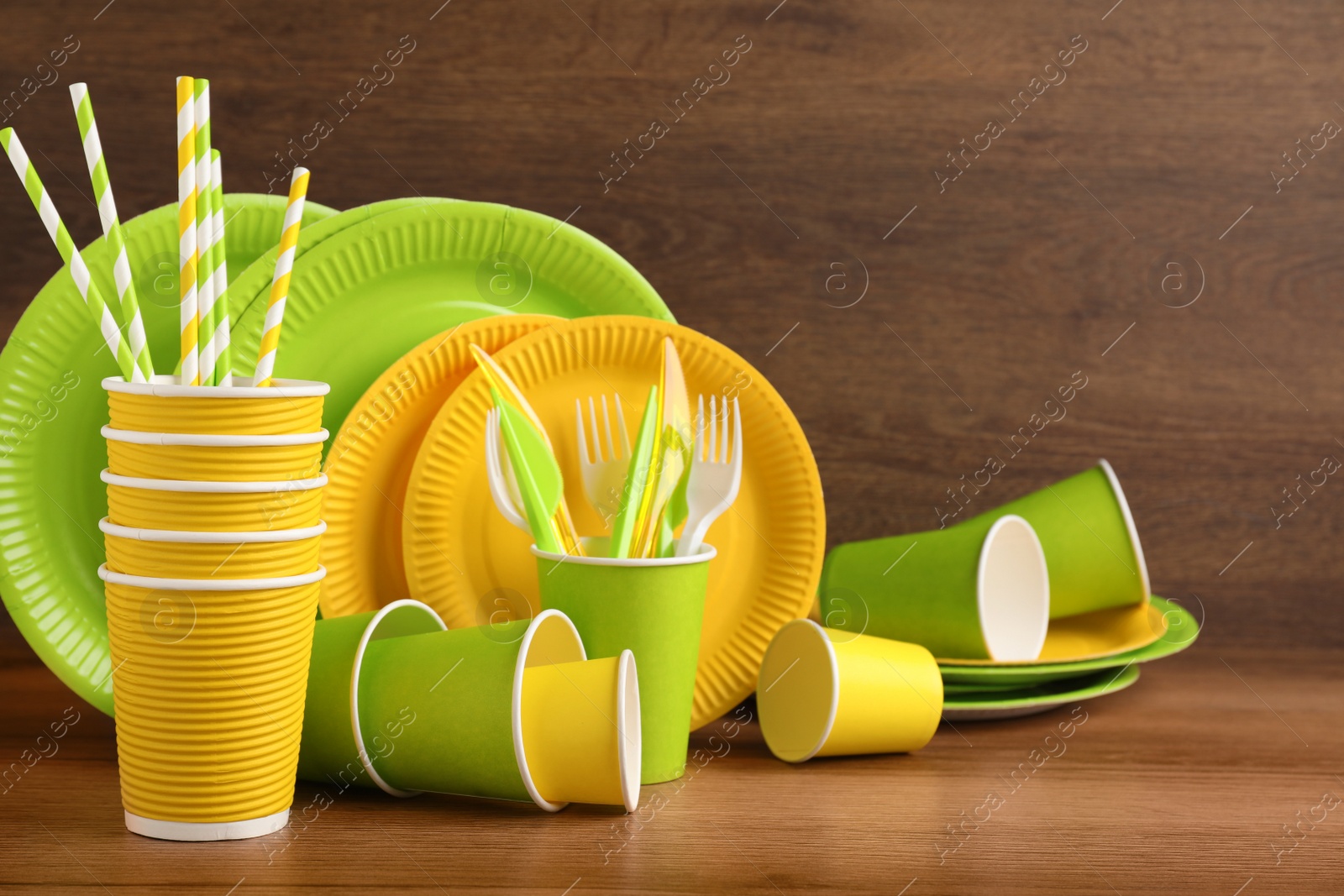 Photo of Set of bright disposable tableware on wooden table