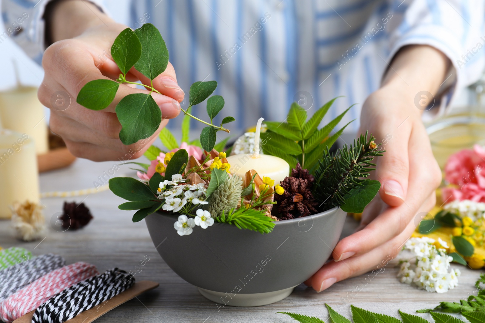 Photo of Woman making floral composition with candle at wooden table, closeup. Master class in handmade craft