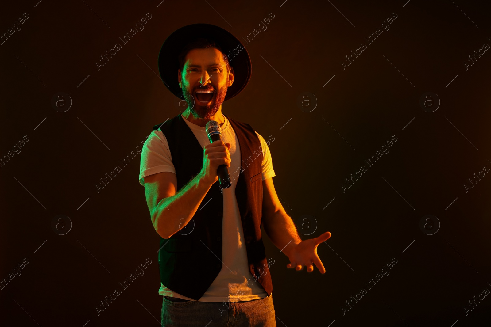 Photo of Handsome man with microphone singing in neon lights on dark background